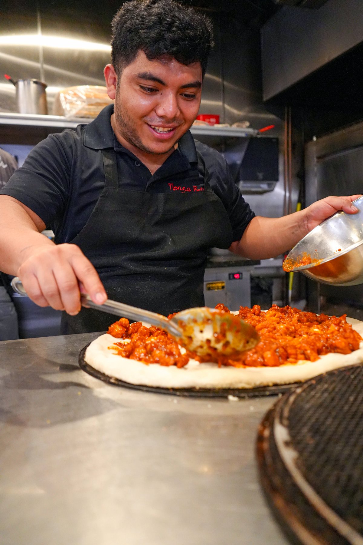 A pizza maker topping a pie on the line