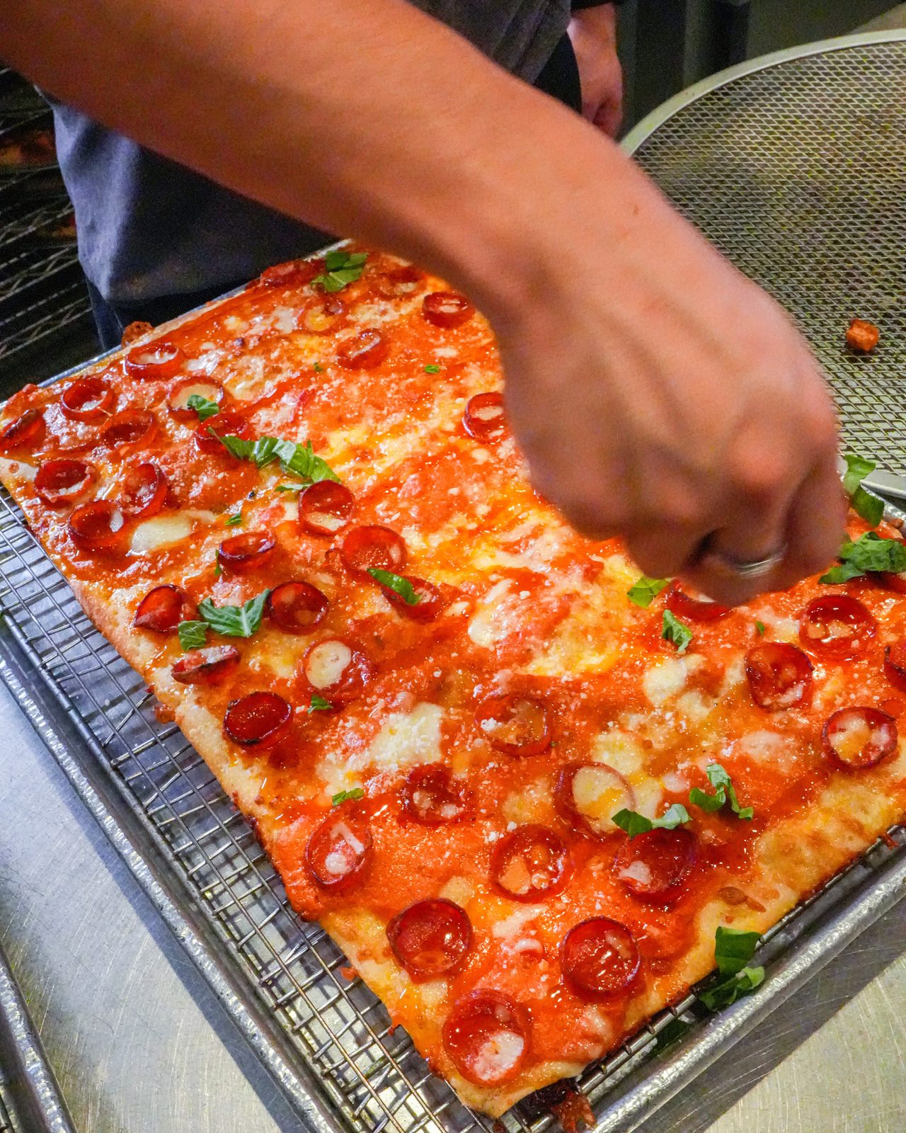 Fresh basil going onto a pepperoni Sicilian