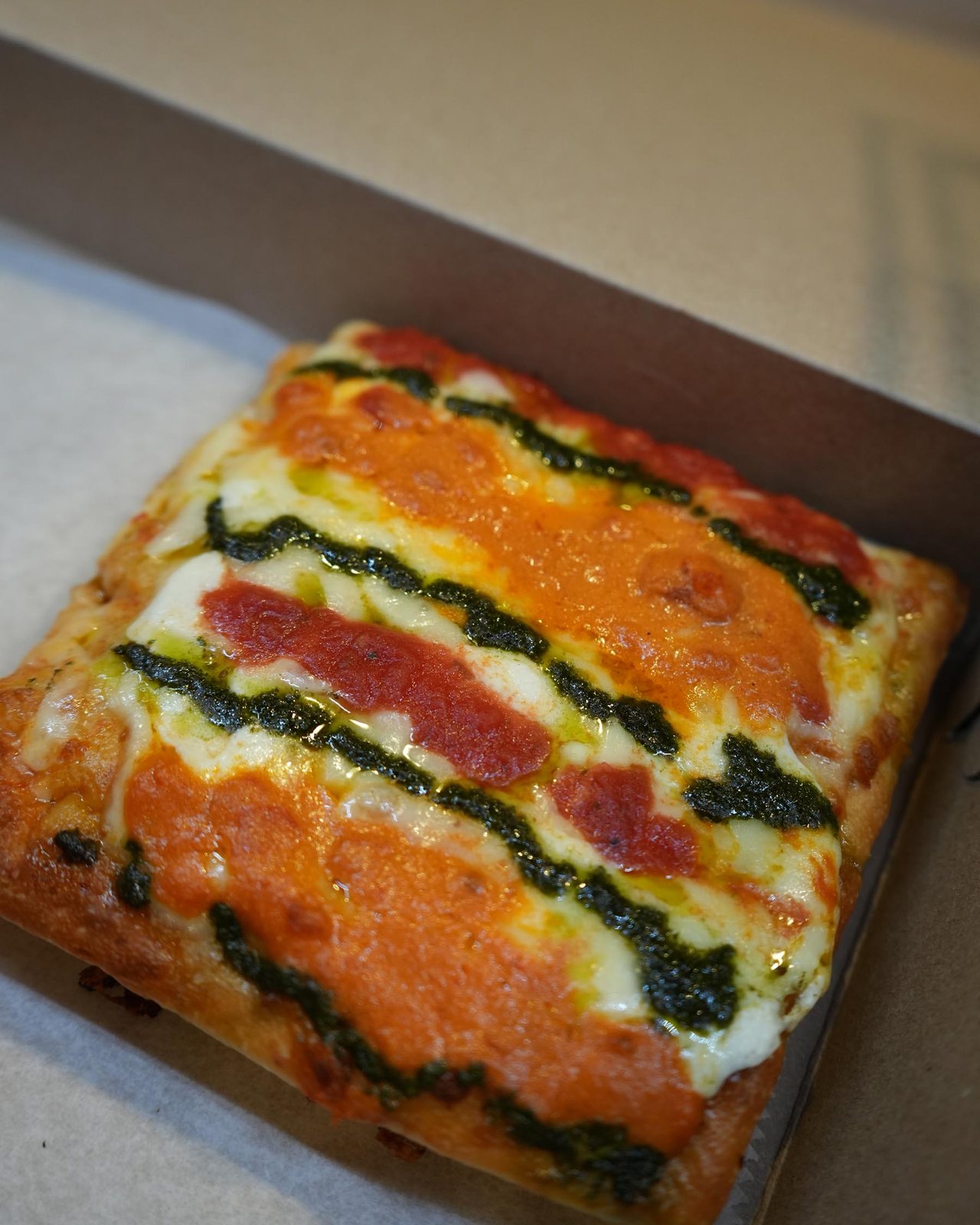 Square pie striped with pesto, red sauce and mozzarella