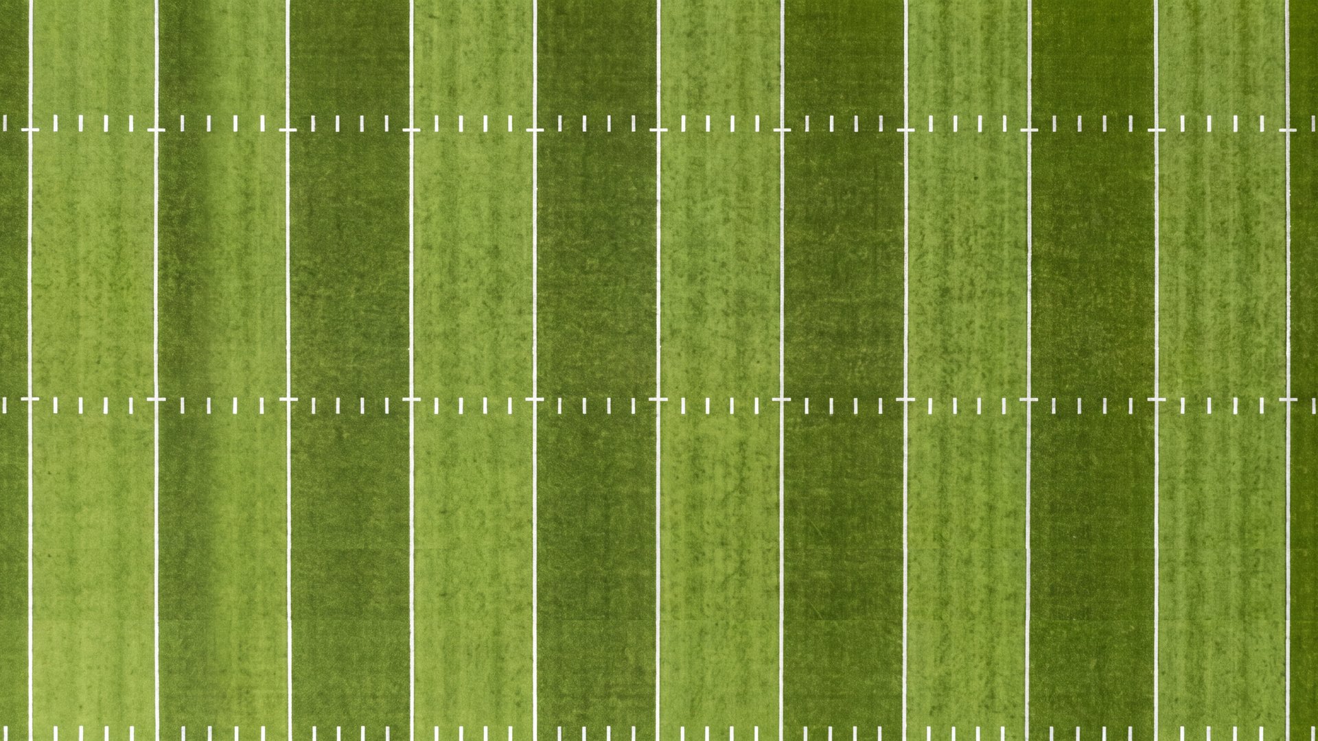 A football field seen from above, yard lines and hash marks on the grass