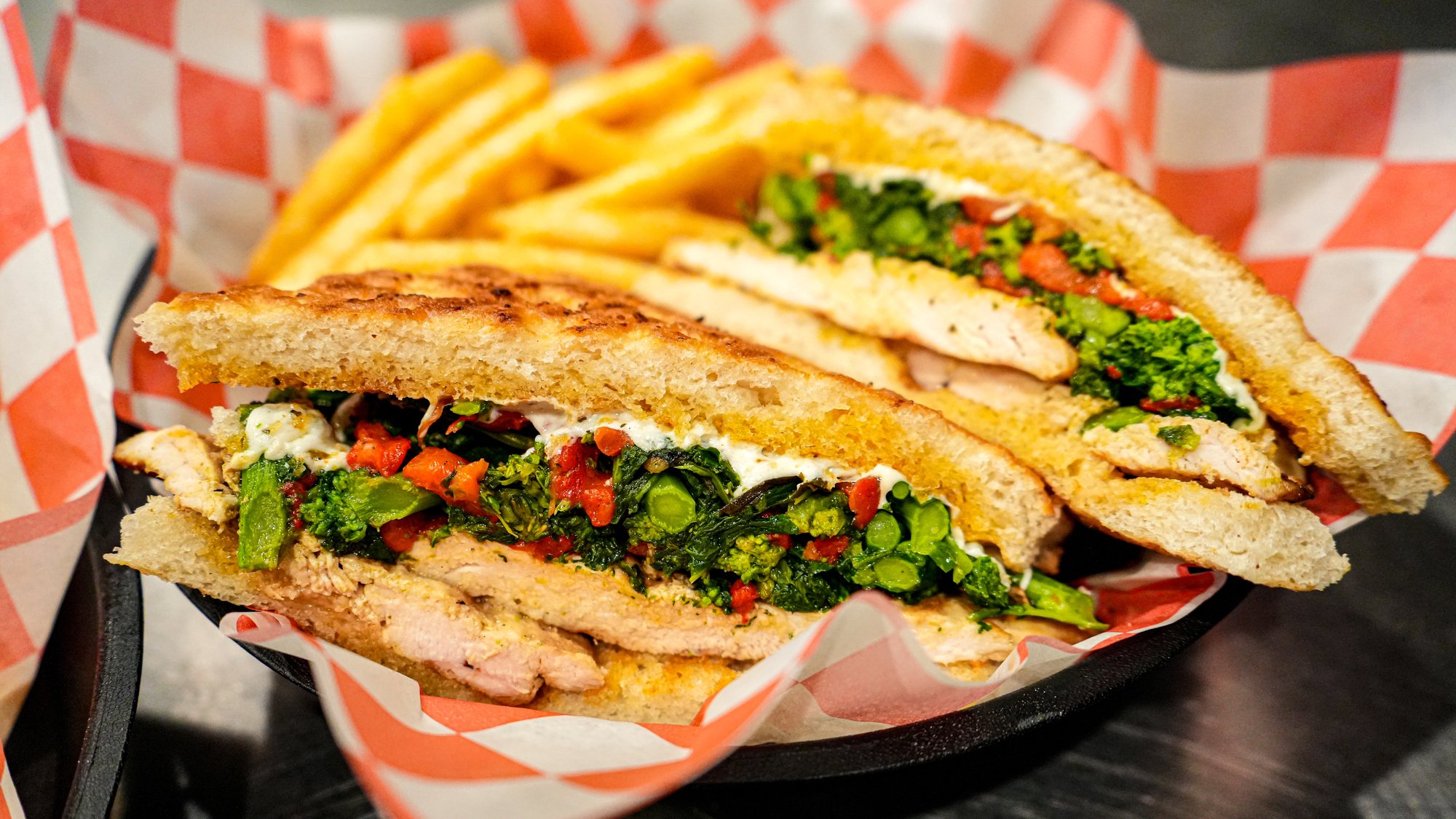 A grilled chicken panini with broccoli rabe and roasted peppers, cut and served with fries