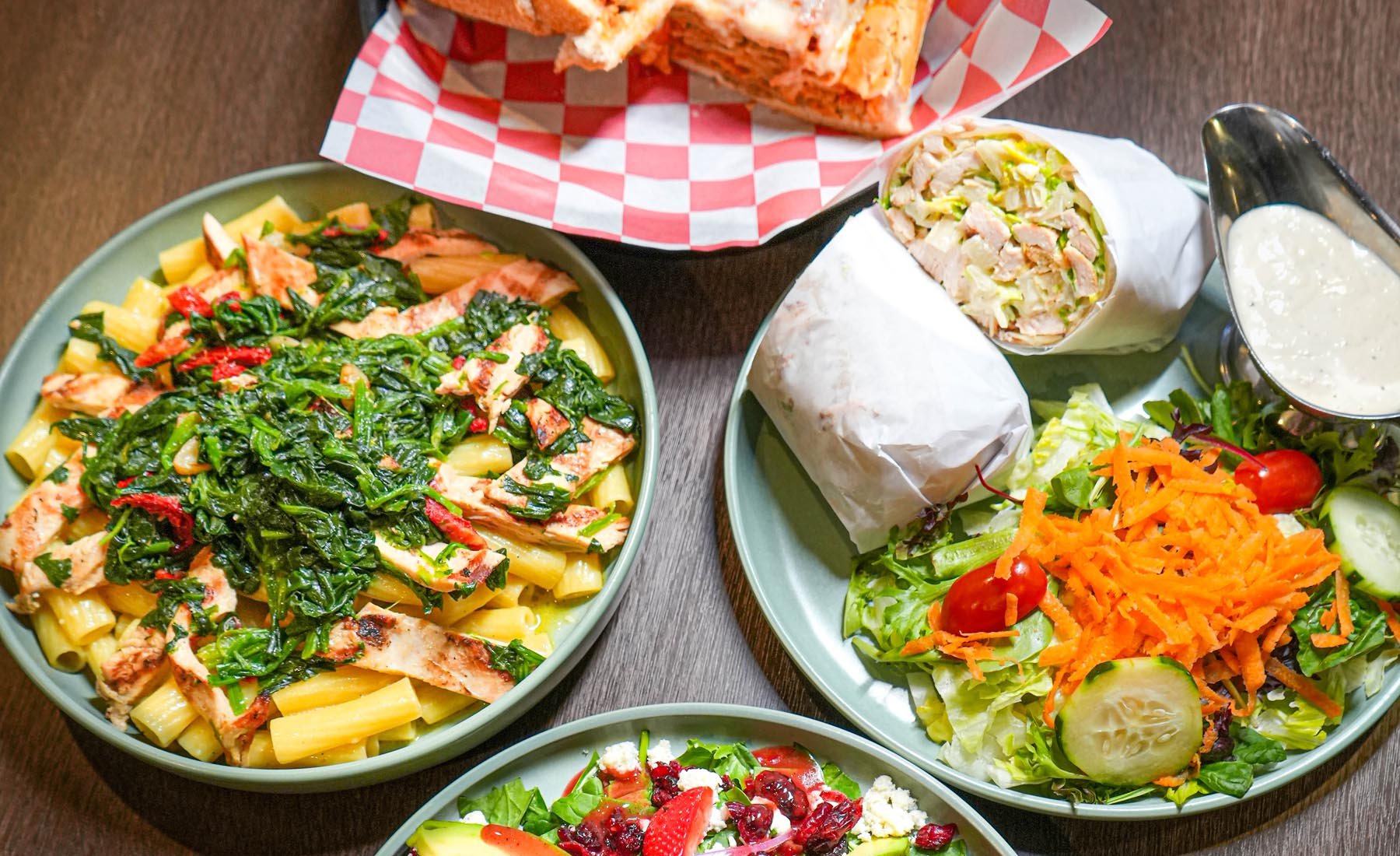 A lunch spread of a panini, a wrap and three salads